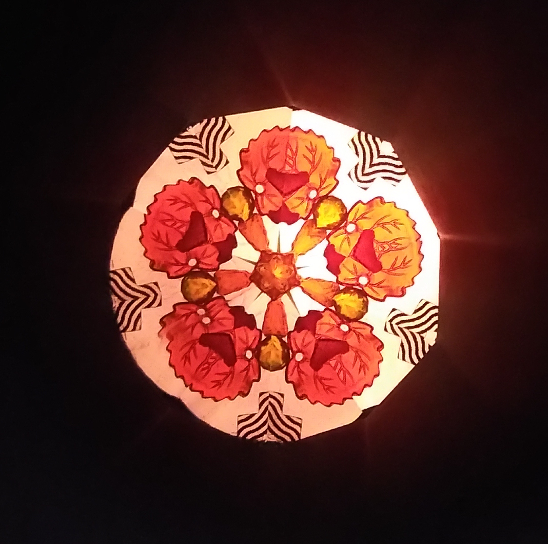 Fleur composée de fleurs orange. Un cercle au centre est relié à des pistils qui s'étendent entre les pétales. Le pourtour est lumineux. 5 décorations en forme de trèfle noir aux contours fins